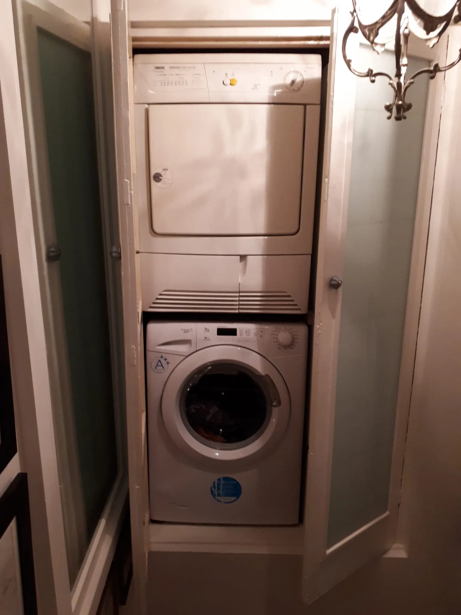 Stacked front-loading washing machine and dryer inside a narrow closet with two folding doors partially open