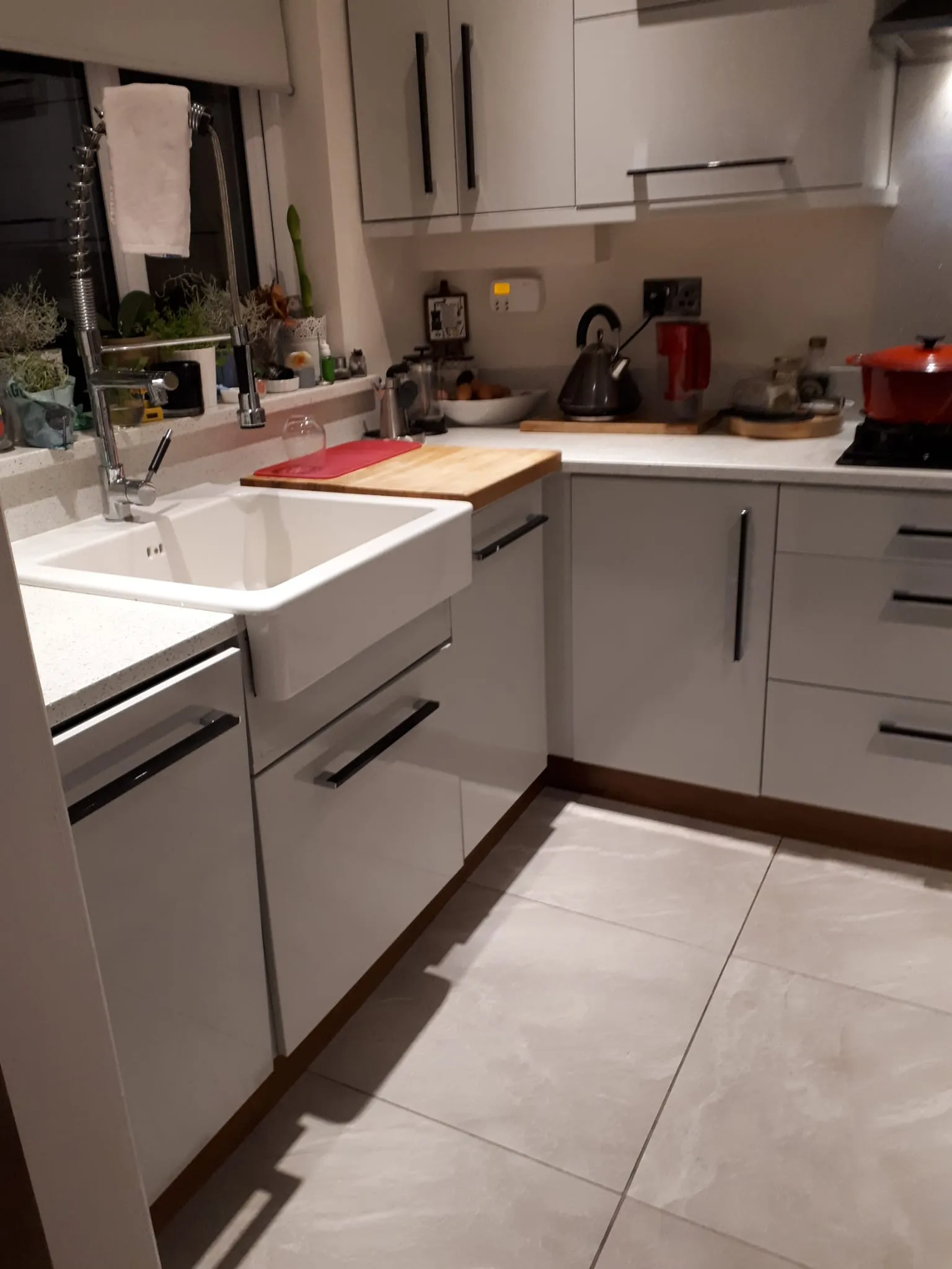 Kitchen corner with a white sink and tall spring faucet, countertop with cutting board, kettle, cabinets and a red pot on the hob