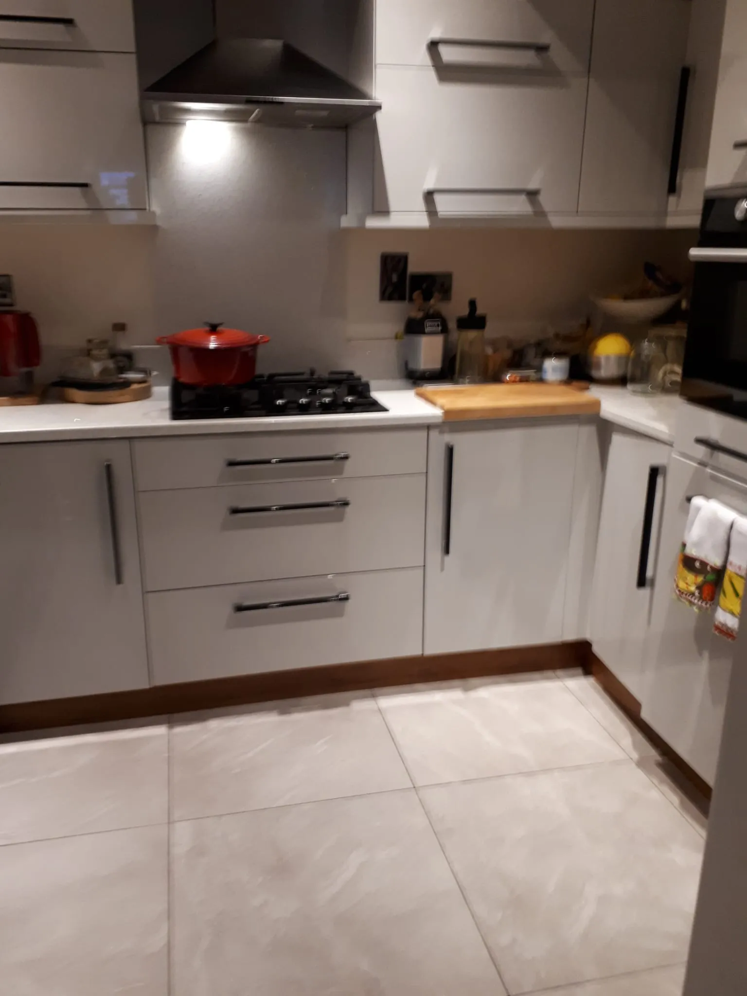 Kitchen with a gas stove and range hood, white cabinets, a red pot on the stovetop and a countertop with a cutting board and small appliances.