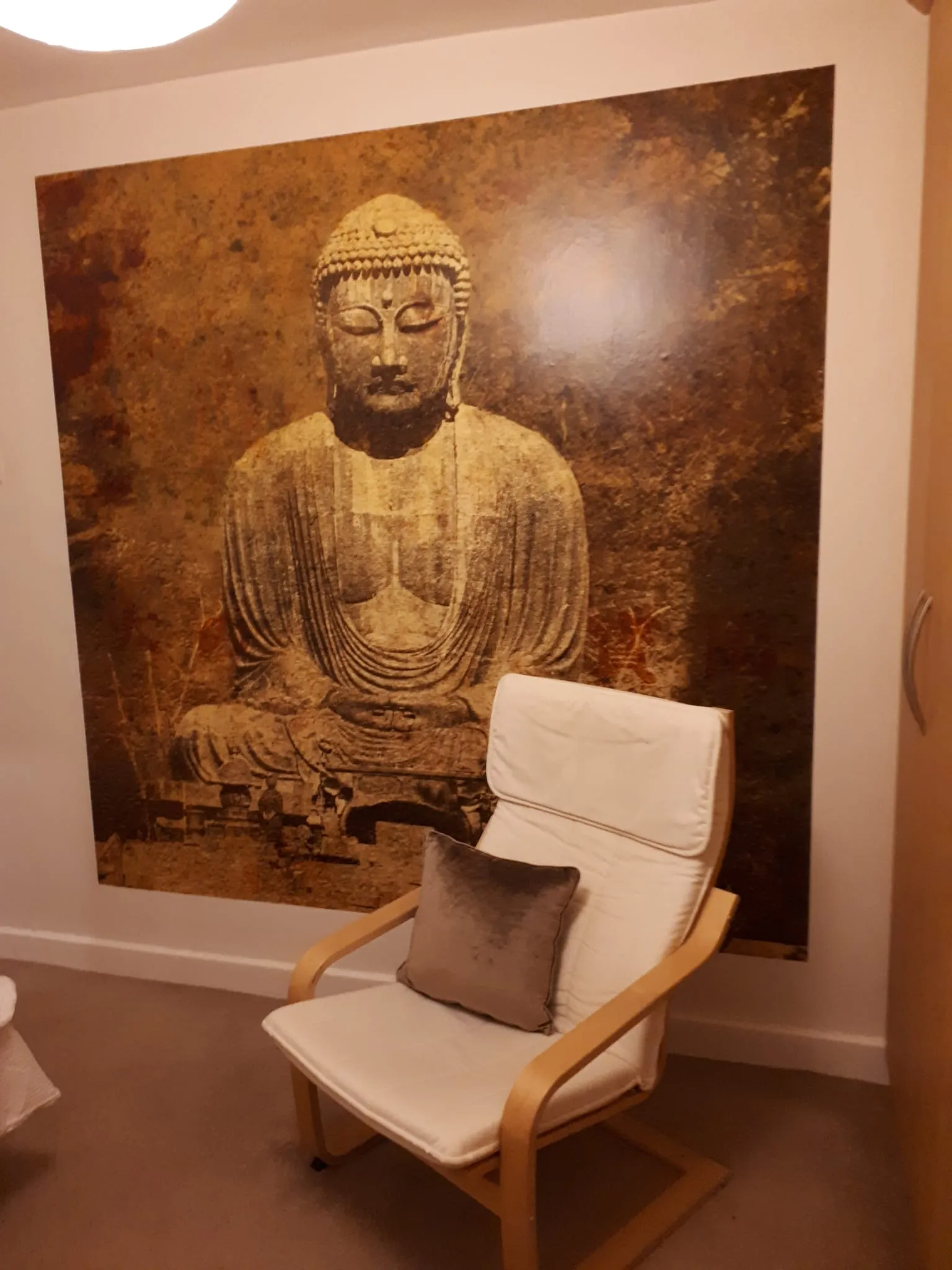 Living room with a white armchair and cushion placed in front of a large Buddha wall mural