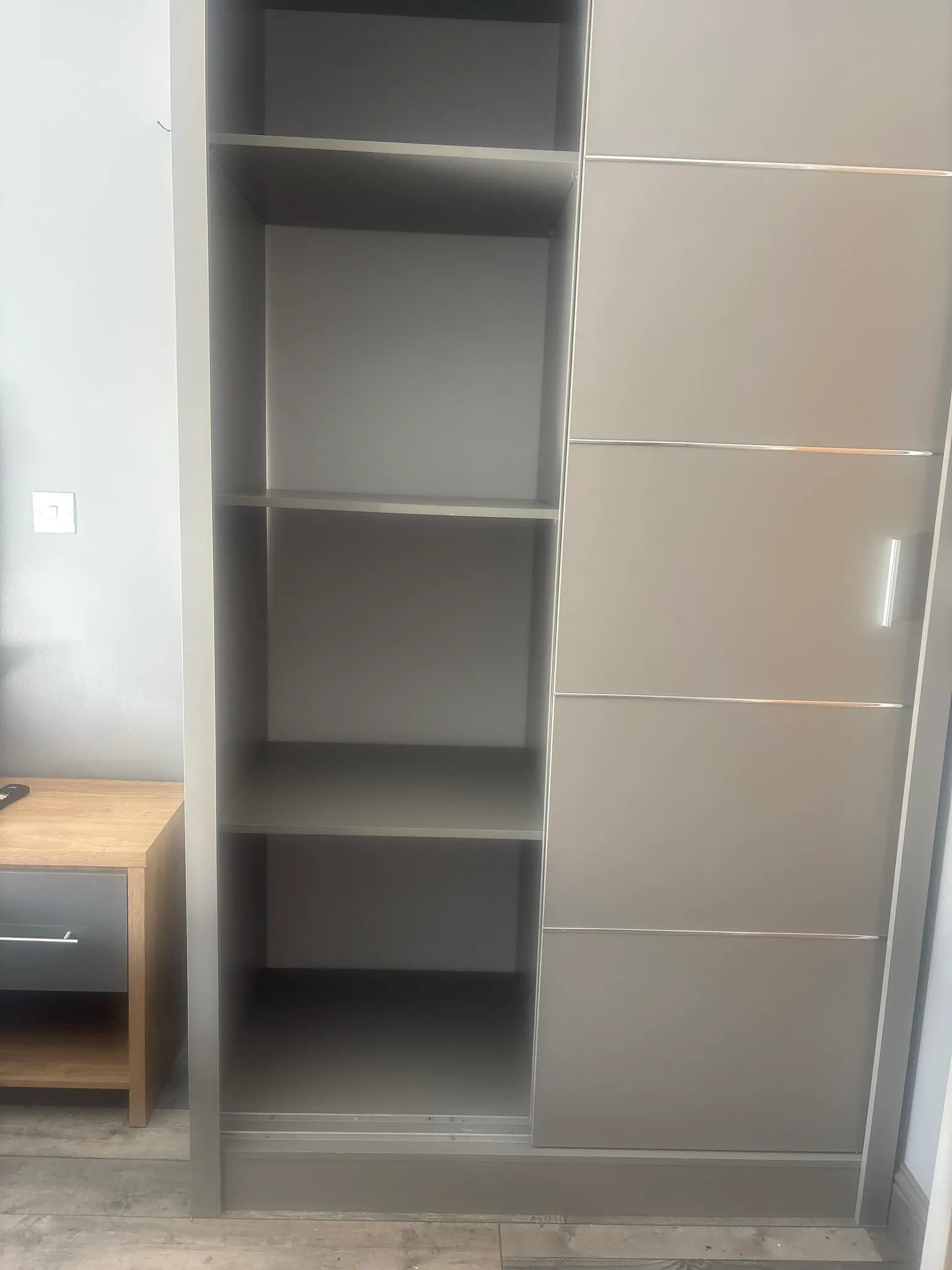 Built-in wardrobe with open shelving on the left and a closed sliding door panel on the right, small bedside table visible at left edge.