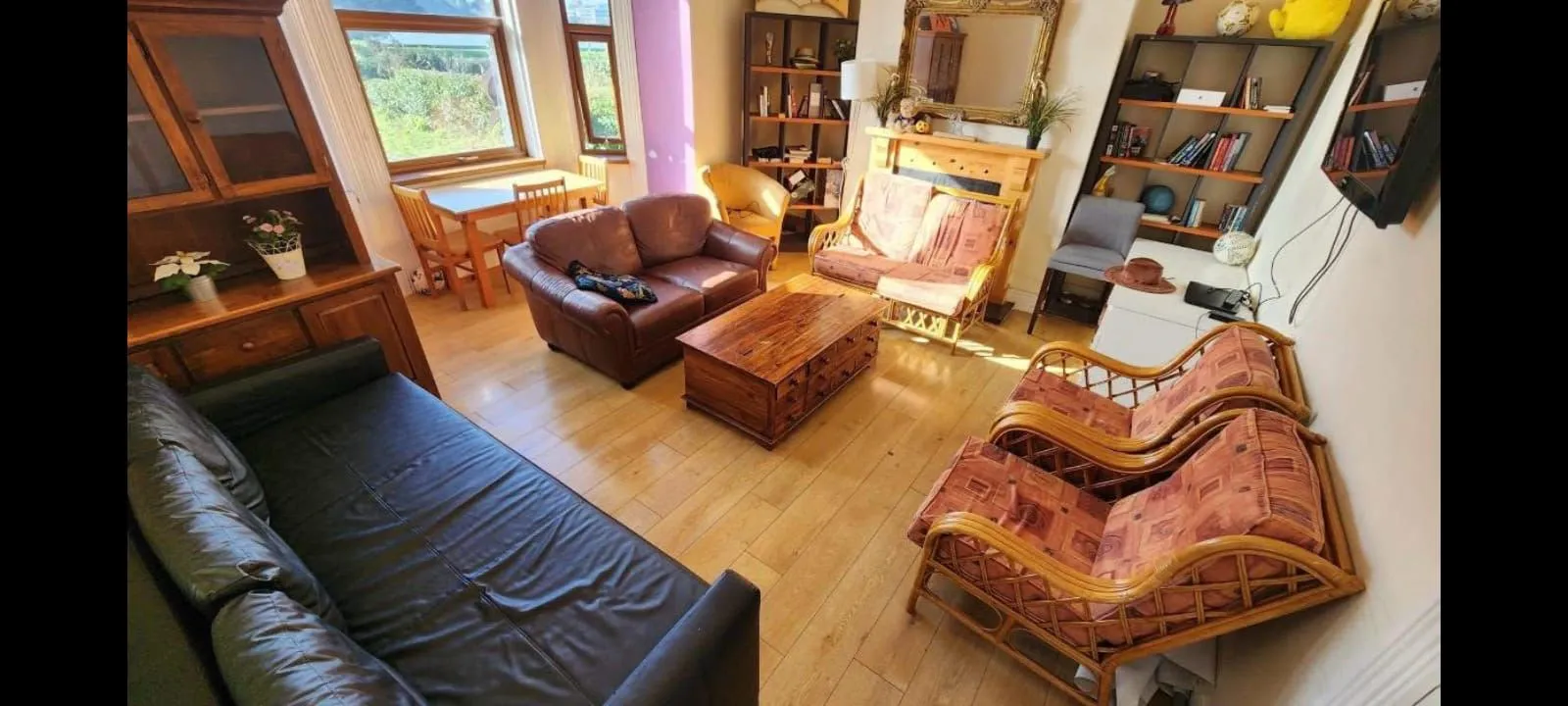 Living room with multiple sofas and armchairs, a central wooden coffee table, bookshelves, dining table by two windows, and a wall-mounted TV.
