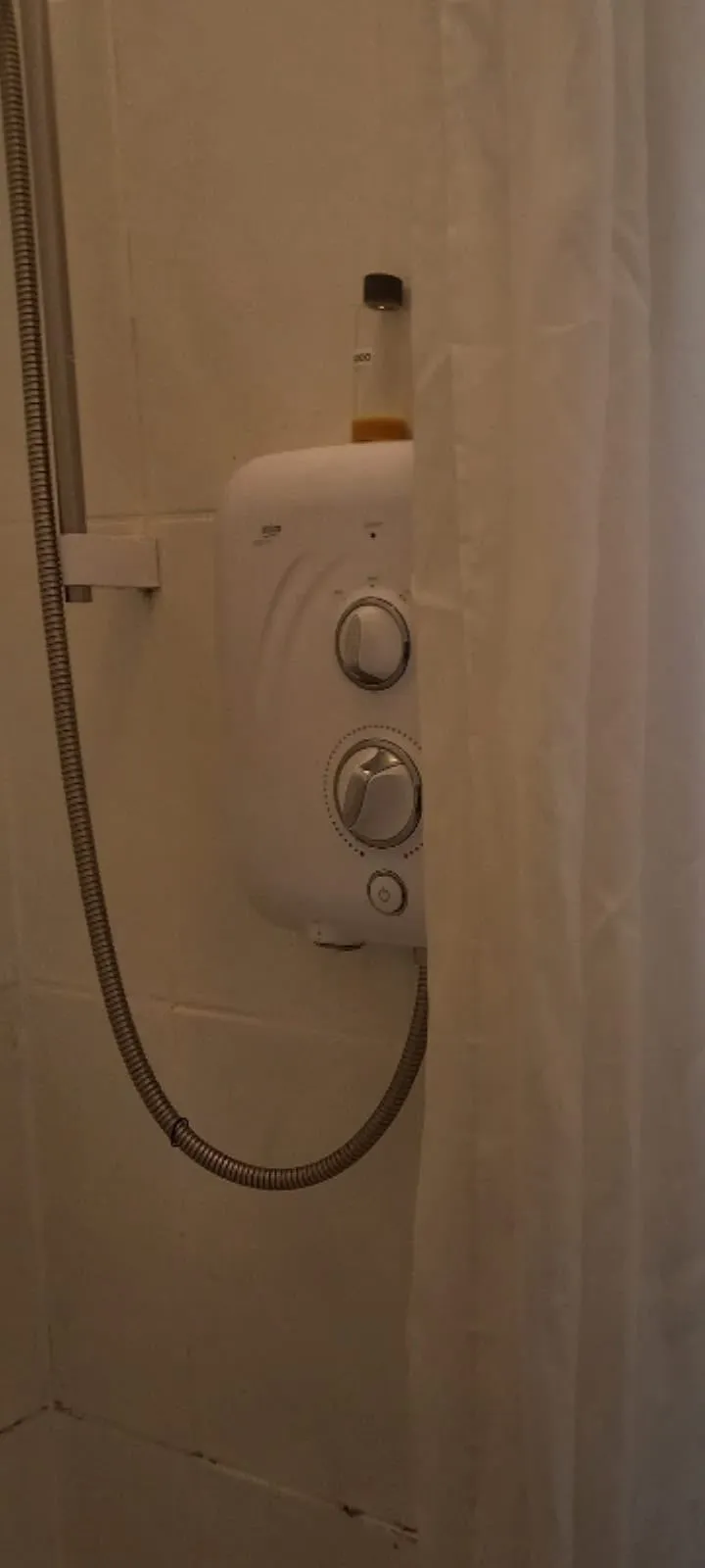 Bathroom shower area with an electric shower unit, flexible metal hose and a partially closed shower curtain.