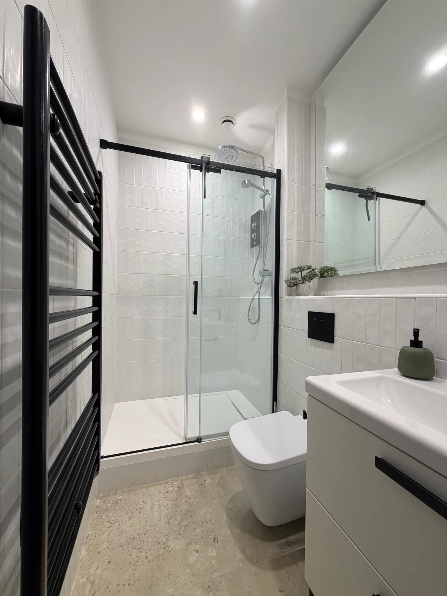 Bathroom with a glass-enclosed shower and rainfall showerhead, wall-mounted towel radiator, toilet, sink and mirror.