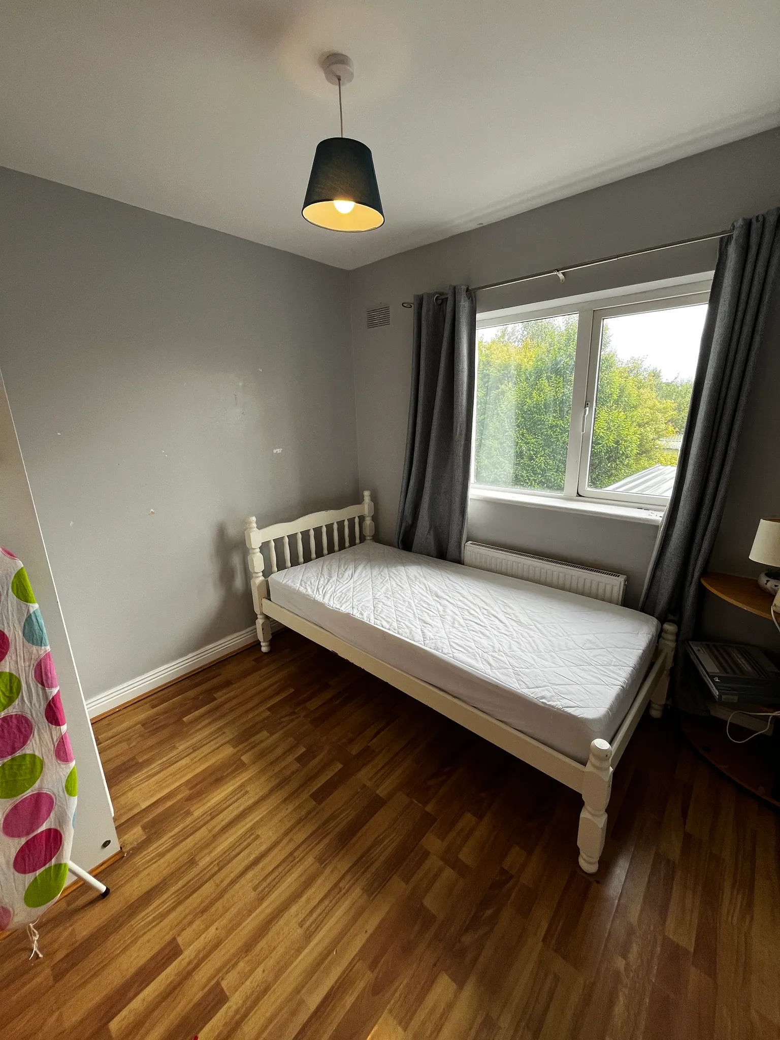 Bedroom with a single bed, window with curtains, radiator under the window, bedside table and pendant ceiling light