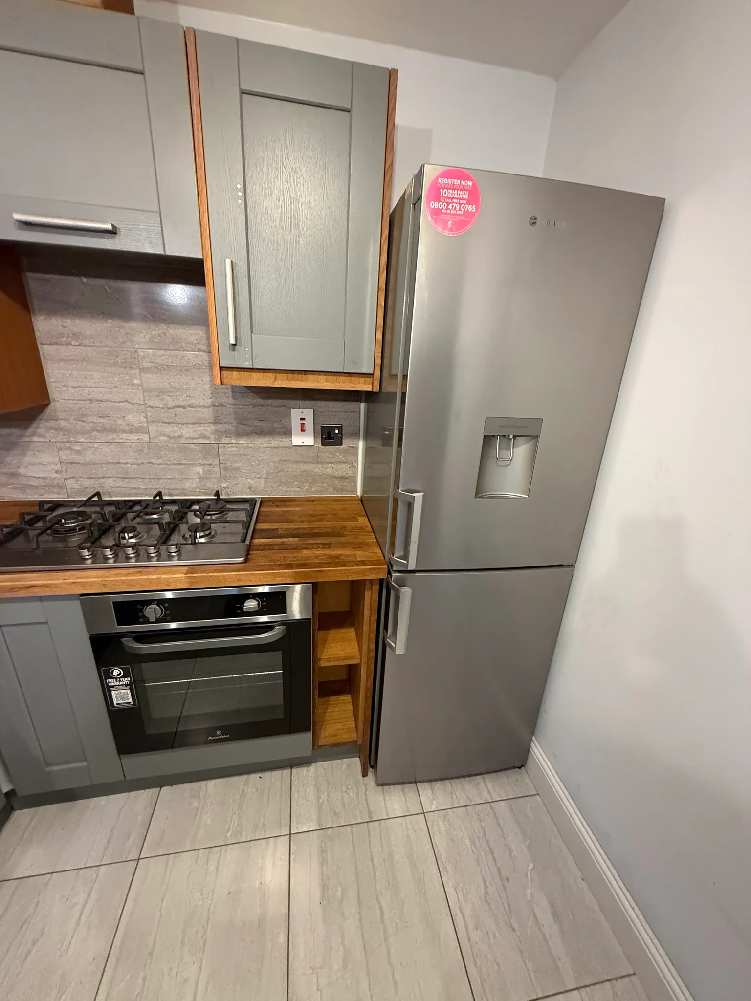 Kitchen corner with a stainless steel refrigerator, wooden countertop, gas hob, oven and upper cabinet.