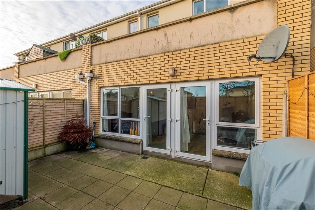 Rear paved courtyard with sliding glass double doors and windows leading to the interior, brick exterior wall, fenced sides, and a covered grill