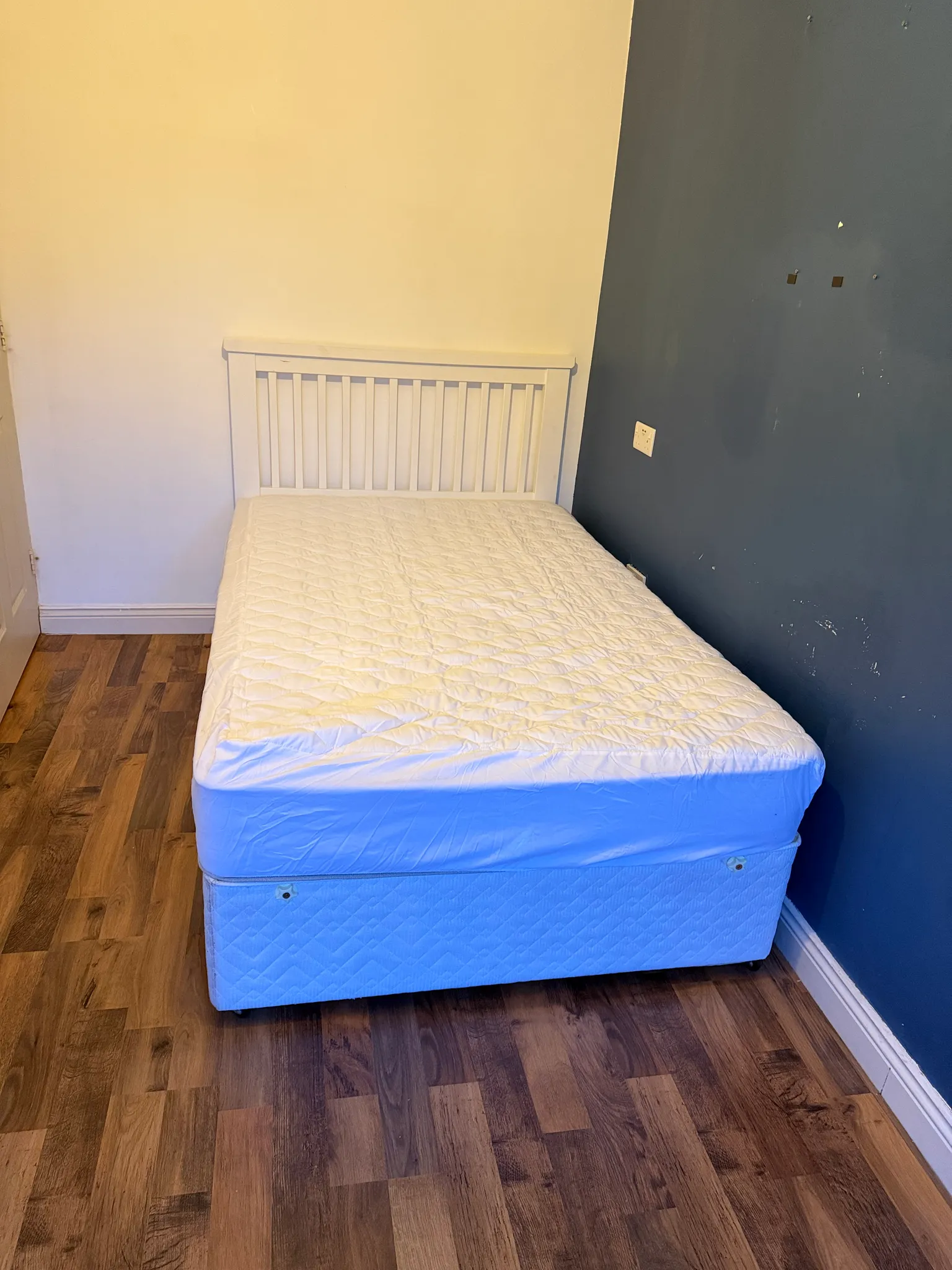 Bedroom with a double bed and white slatted headboard against a white and dark blue wall, hardwood floor visible