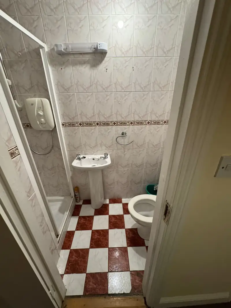 Small bathroom with a pedestal sink, toilet, corner shower and checkered red-and-white tiled floor.