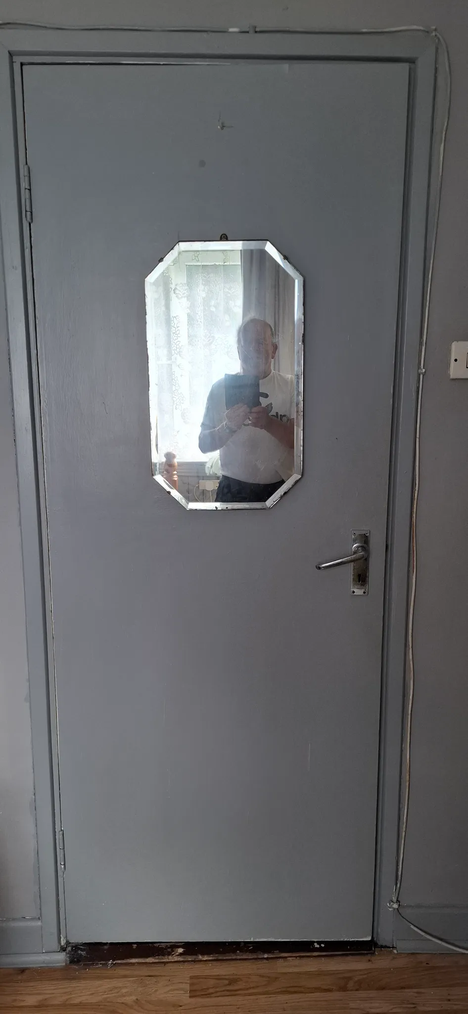 Interior painted door with a small octagonal mirror mounted at eye level reflecting a person, metal handle, and wood floor visible at the bottom