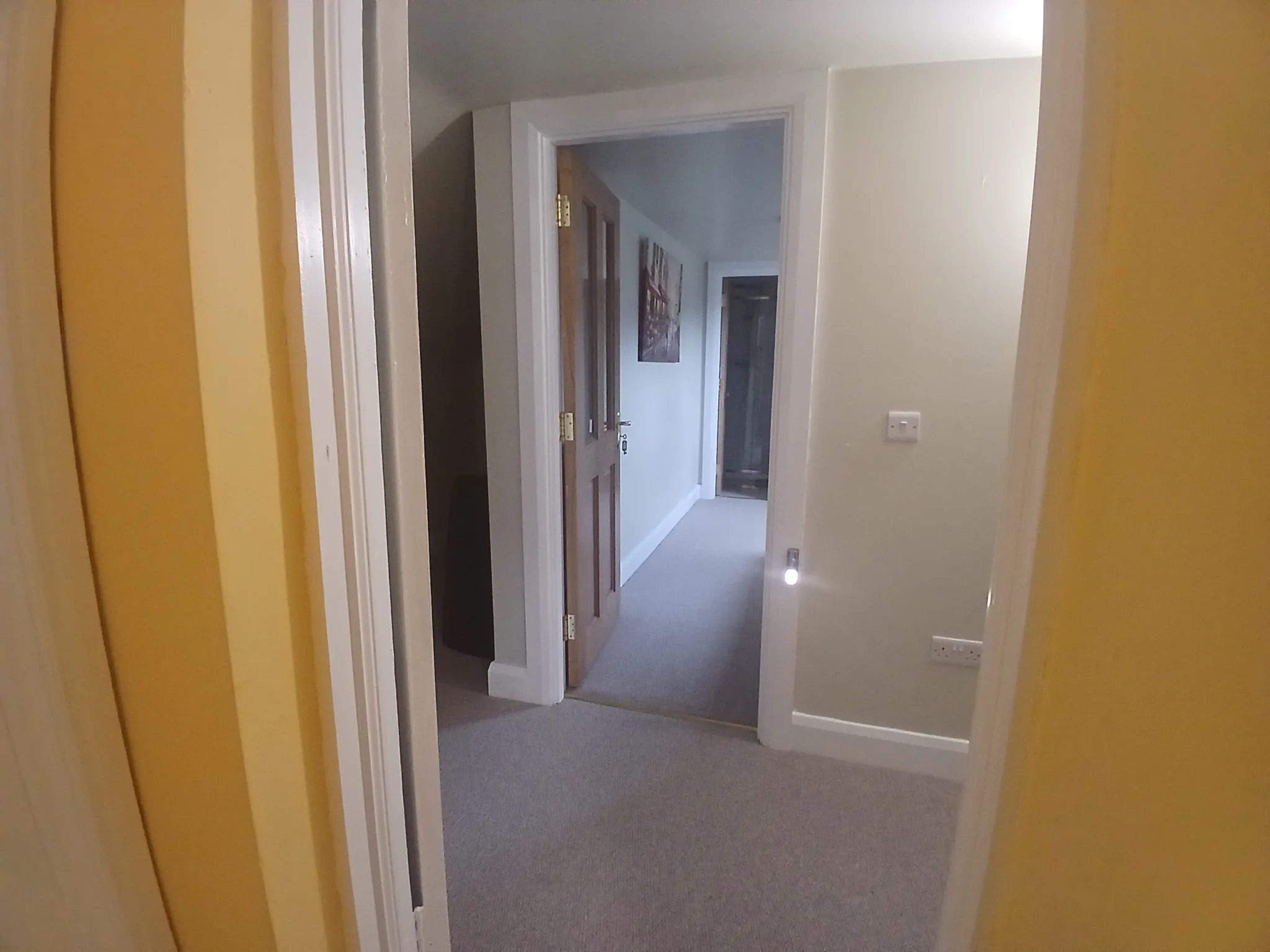Hallway with open wooden doors, beige and white walls, carpeted floor and a small nightlight on the wall.