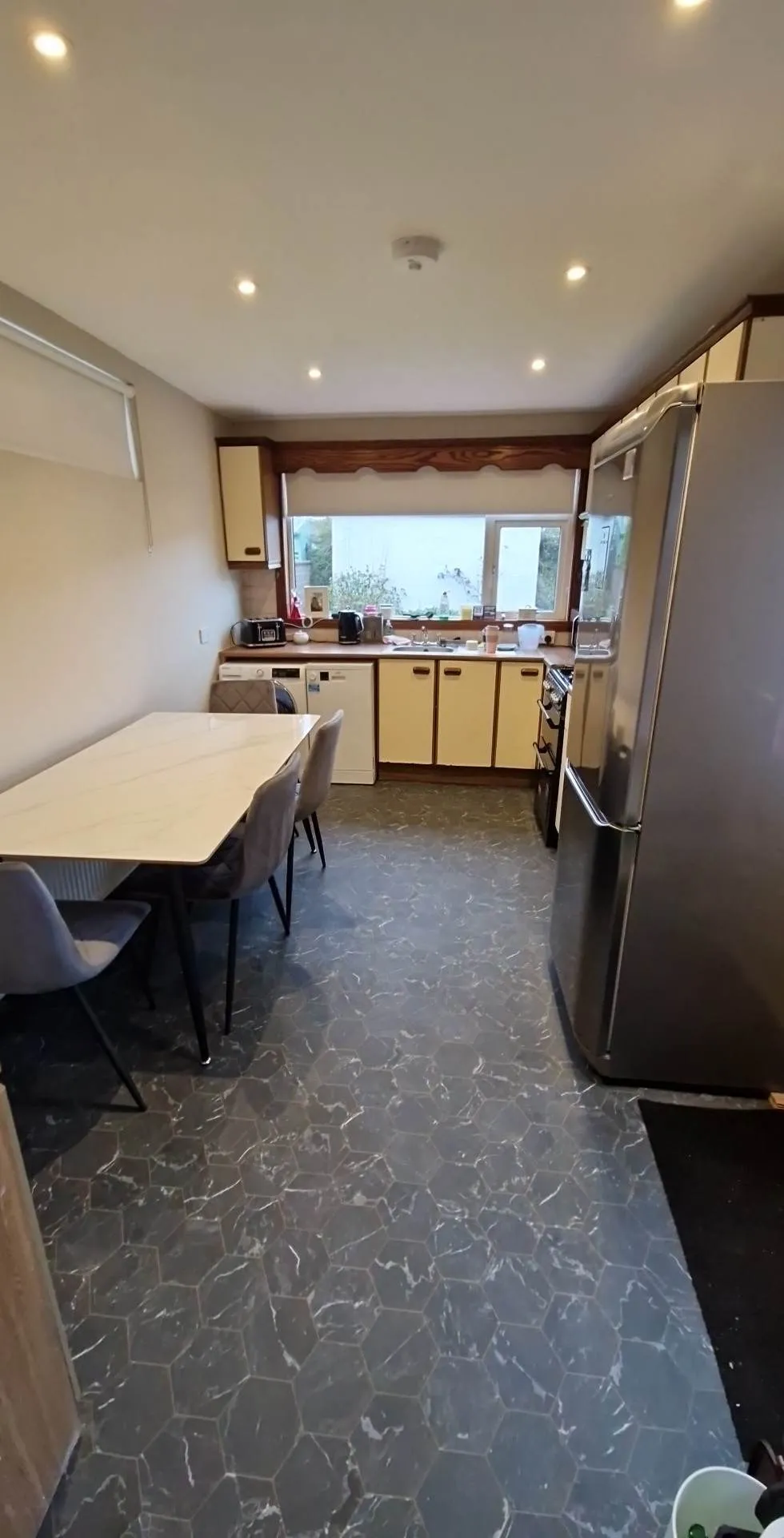 Kitchen with a dining table and four chairs, cabinets and countertop with a sink below a window and a refrigerator on the right.