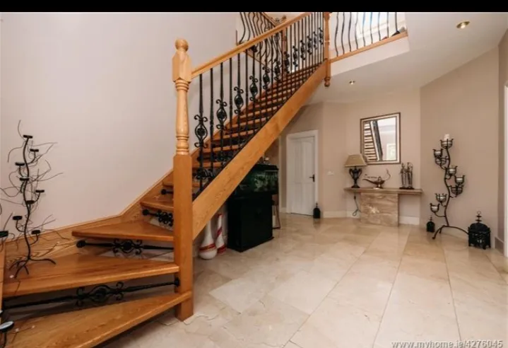 Entry hallway with a wooden staircase with wrought-iron balusters, tiled floor, console table with mirror and decorative candle holders.