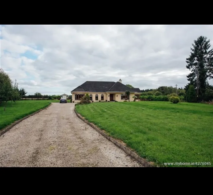 Exterior view of a single-story house at the end of a gravel driveway with a front lawn, car parked near the house, and trees under a cloudy sky.