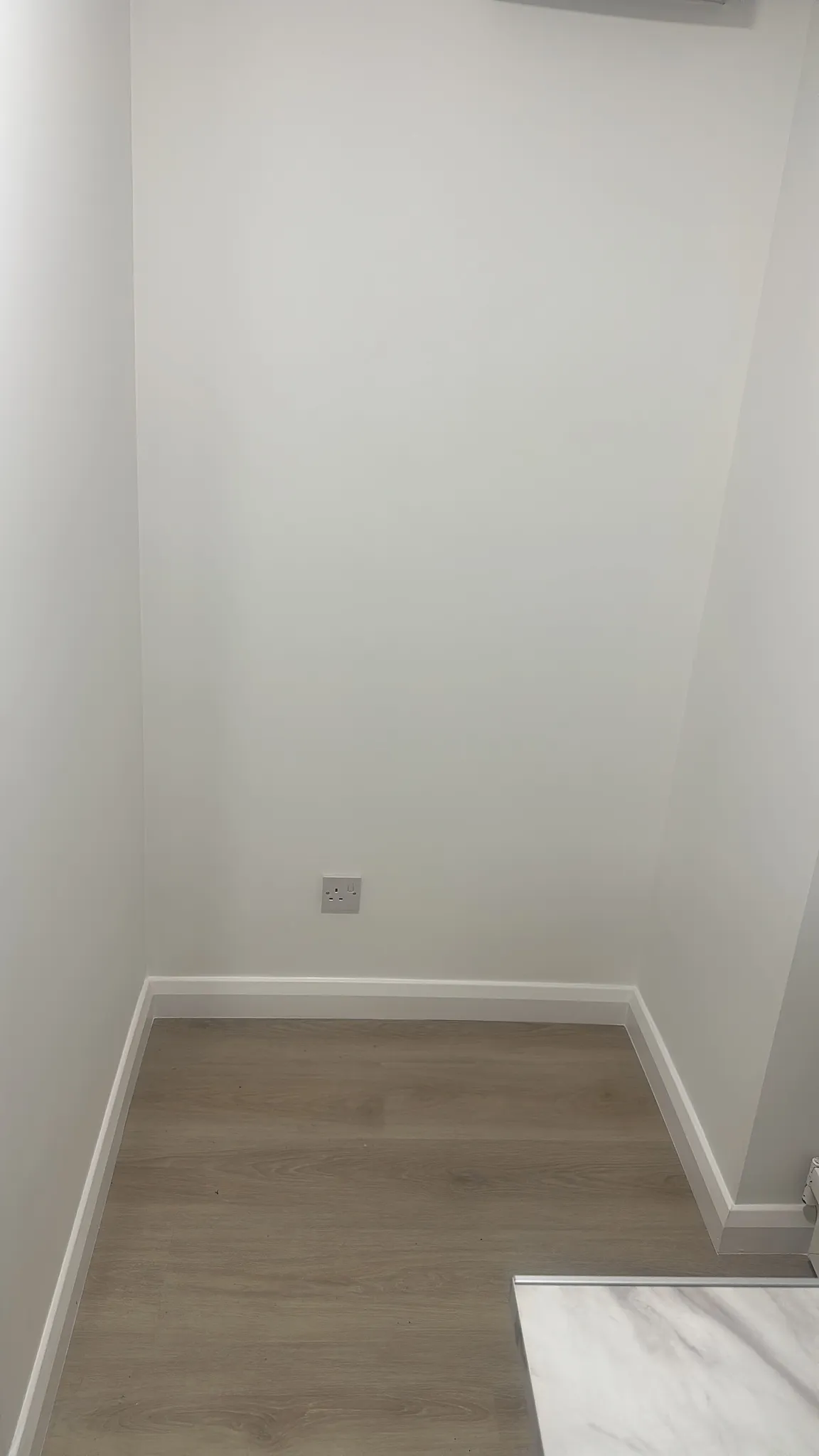 Empty room with white walls, wood-look flooring, white baseboard trim, and a wall outlet