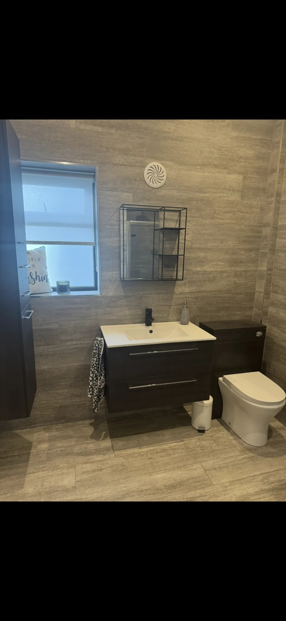 Bathroom with wall-mounted vanity and sink, mirror cabinet above, toilet to the right, and a frosted window to the left.
