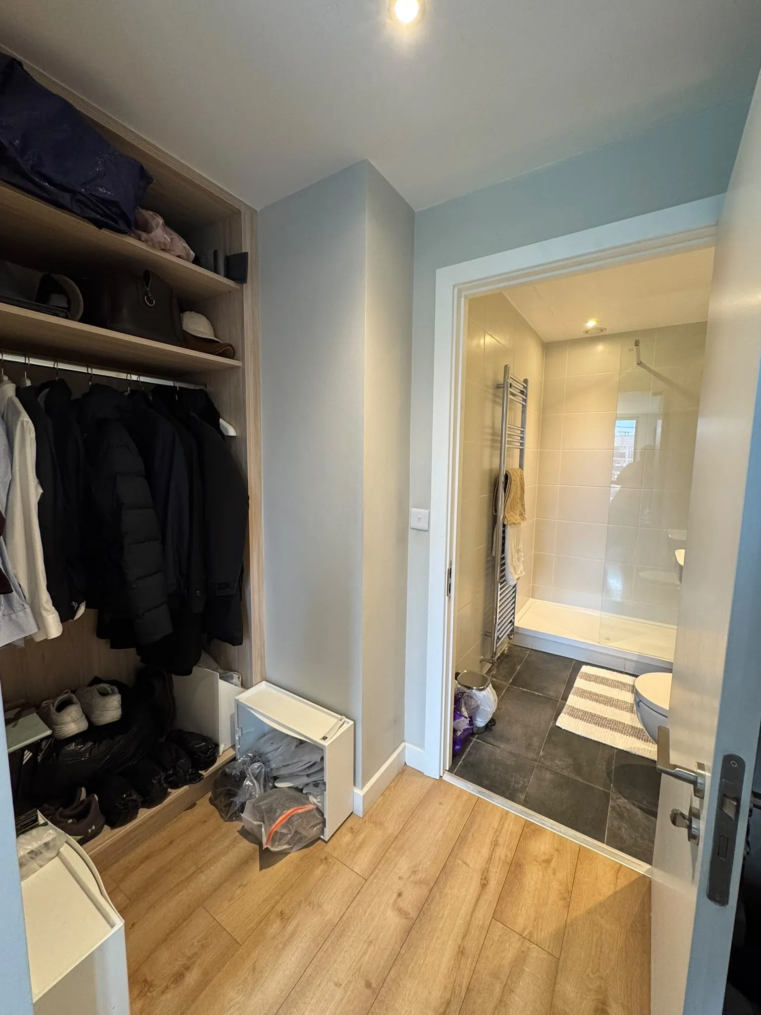 Hallway with a built-in open closet on the left and an open door leading to a tiled bathroom with a shower and towel rail.