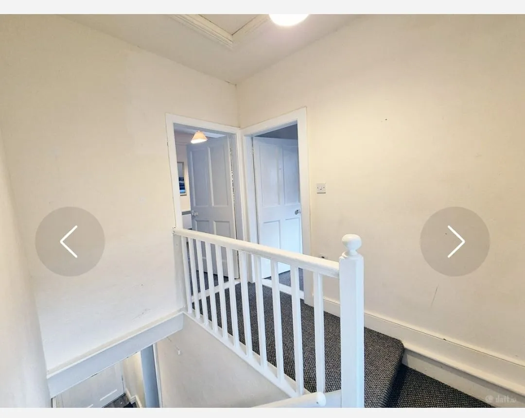 Upper-floor hallway landing with a white wooden banister, carpeted floor, and two open doors leading to rooms