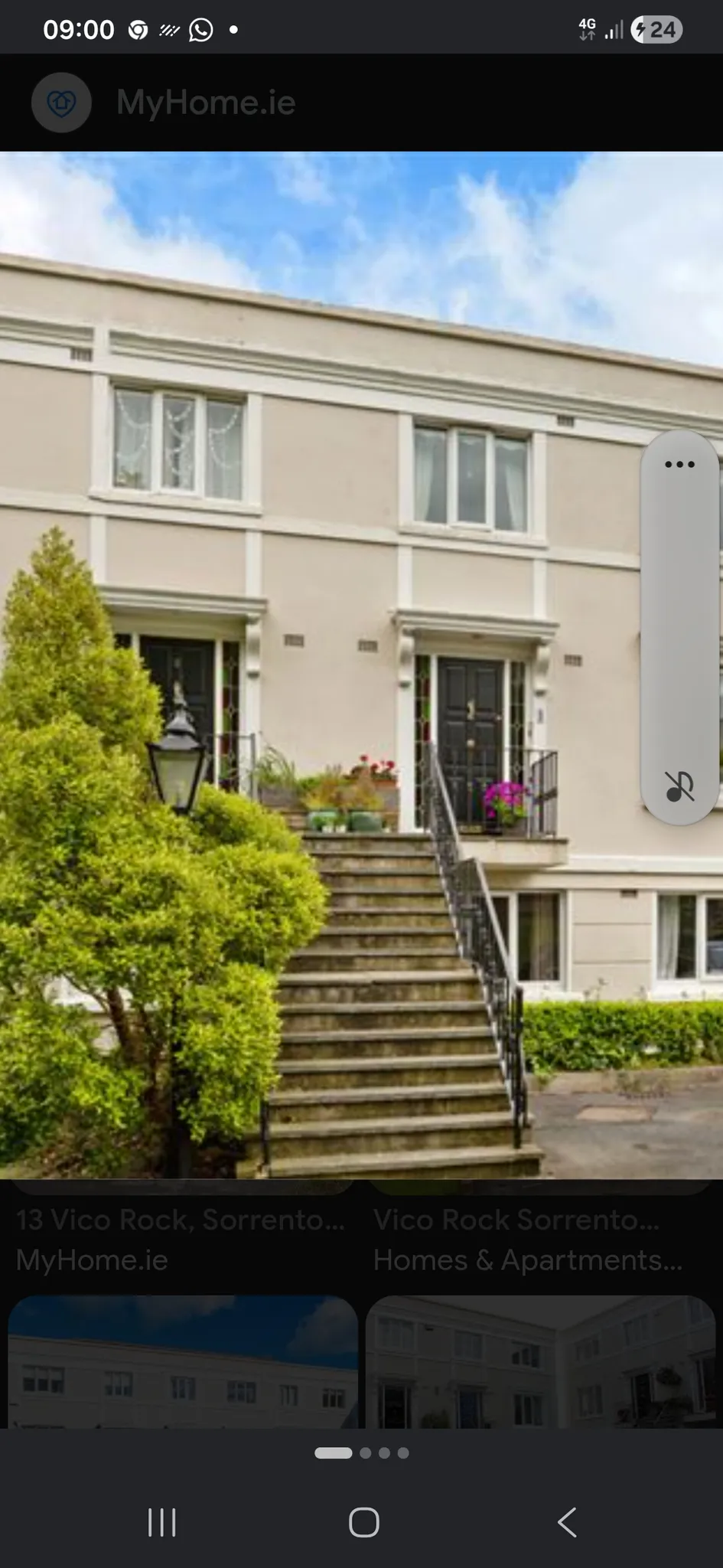 Exterior view of a two-story building with a central stone staircase leading to two black front doors, windows above, metal railings, potted plants and a lamp post to the left.