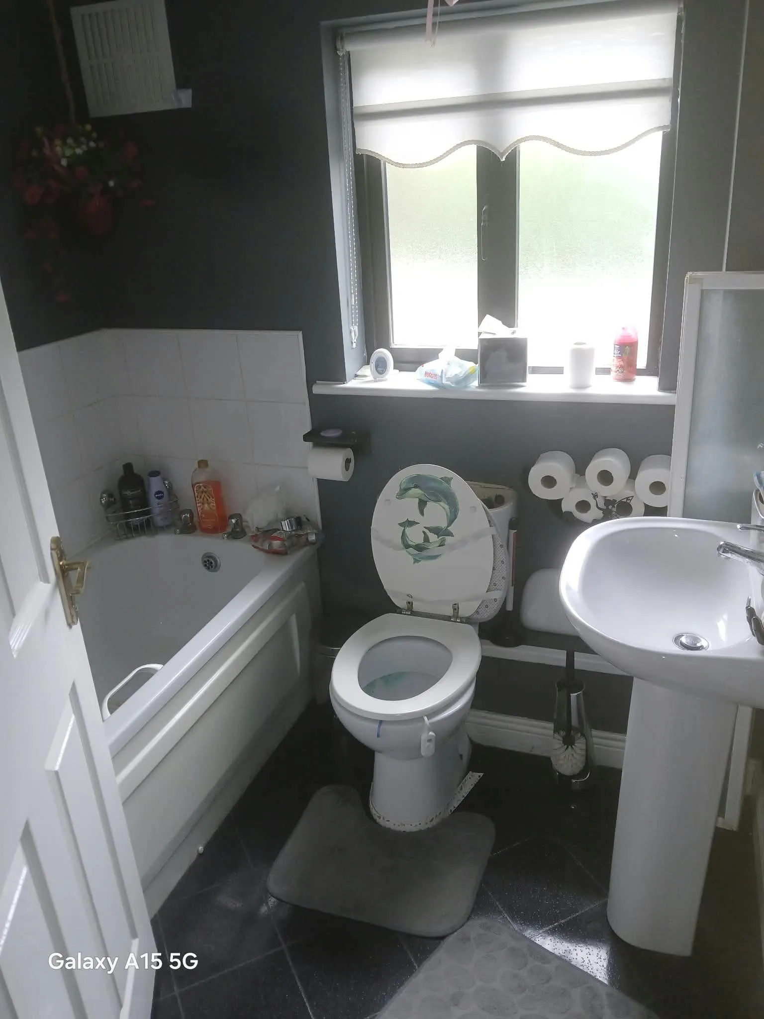 Bathroom with a toilet, pedestal sink, bathtub, and frosted window with a roller blind.
