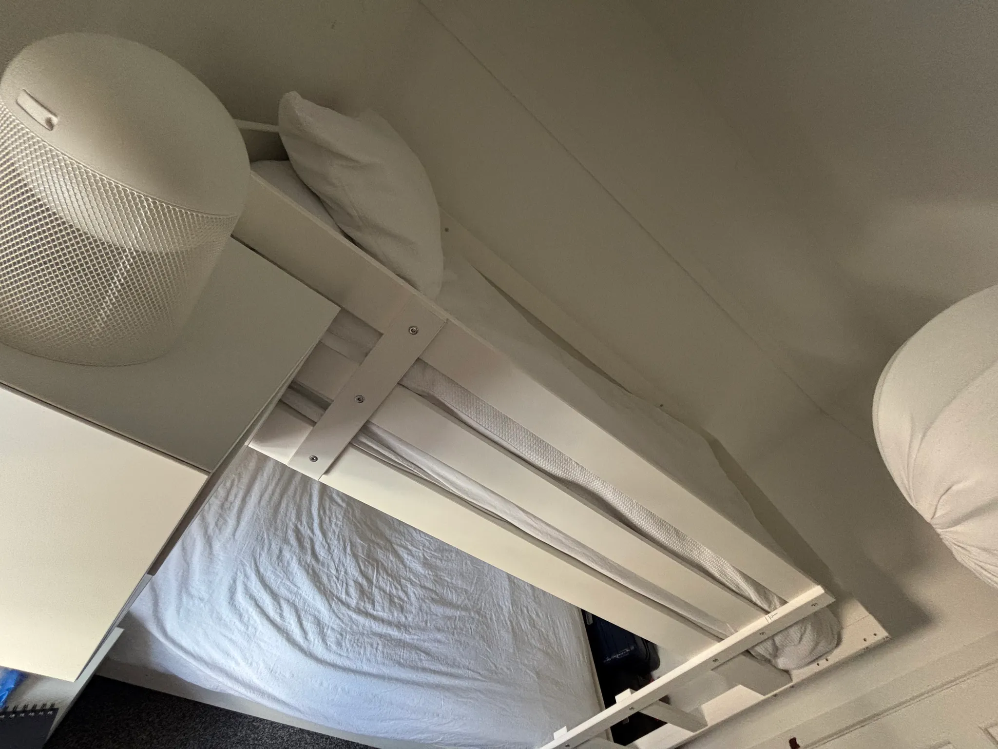Bedroom view of a white bed with guardrail and mattress, white pillow, small bedside lamp and part of a cabinet.