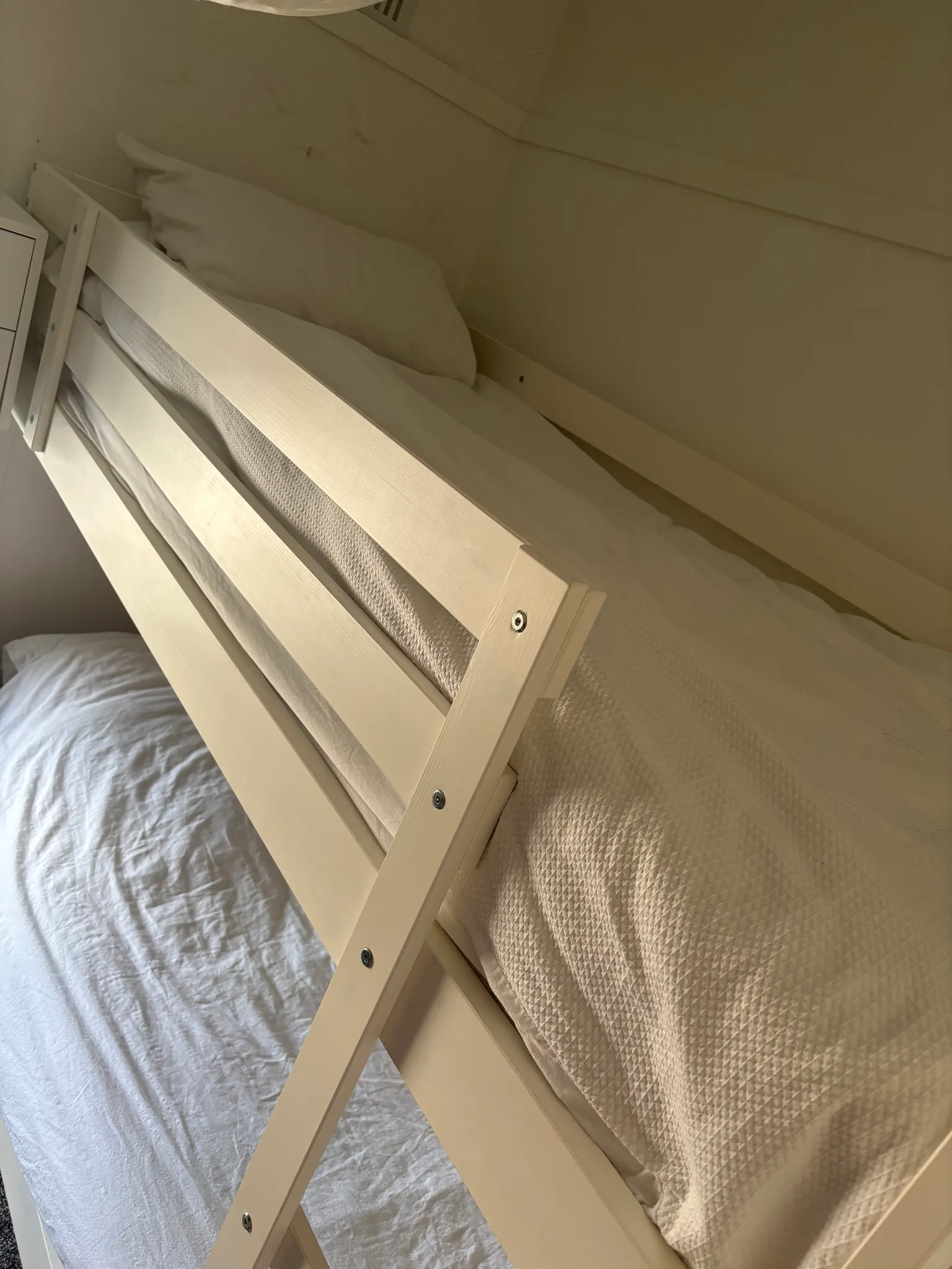 Bedroom with a light-wood bunk bed frame, white bedding and pillows, photographed at an angle