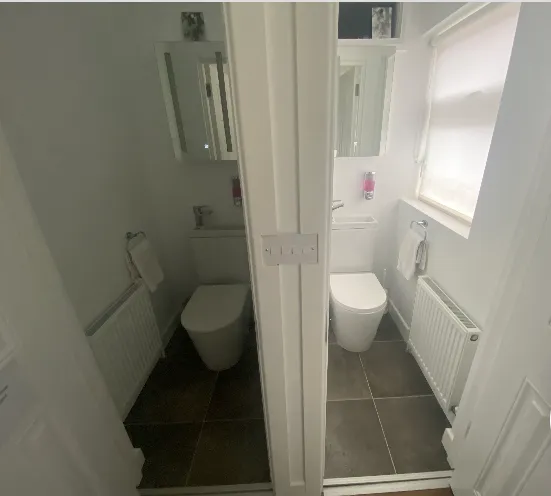 Small bathroom with a toilet, wall mirror, radiator and a window with a blind