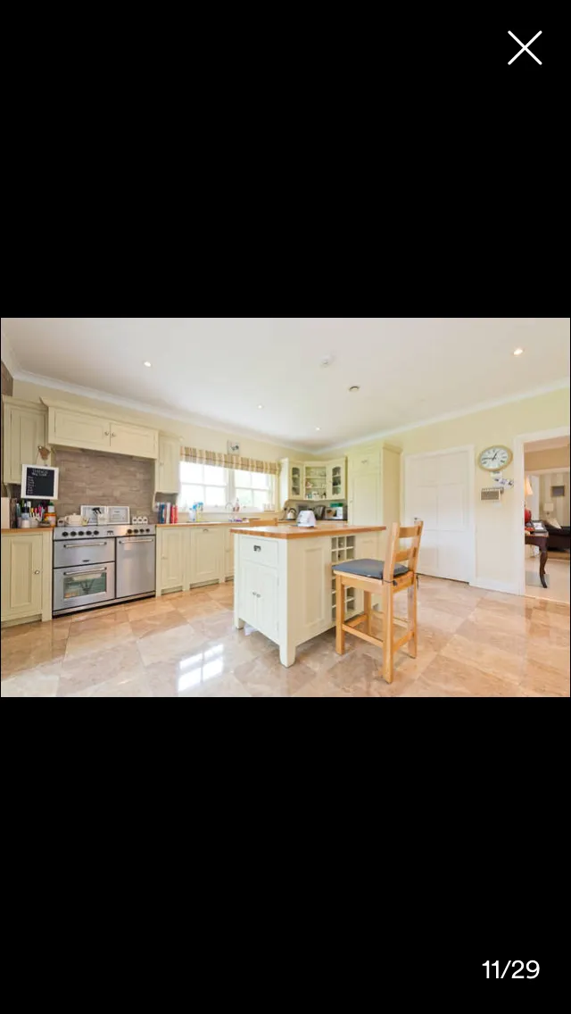 Kitchen with cream-colored cabinetry, stainless steel double oven, central island with seating, terracotta tile flooring, and window with checkered curtains