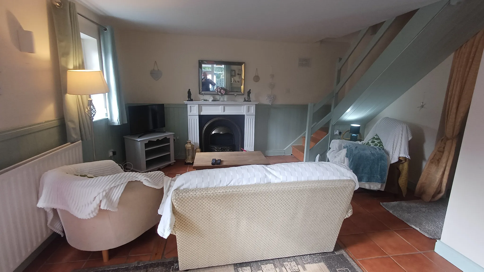 Living room with two sofas and an armchair facing a coffee table, fireplace with a mirror above, television and an interior staircase.