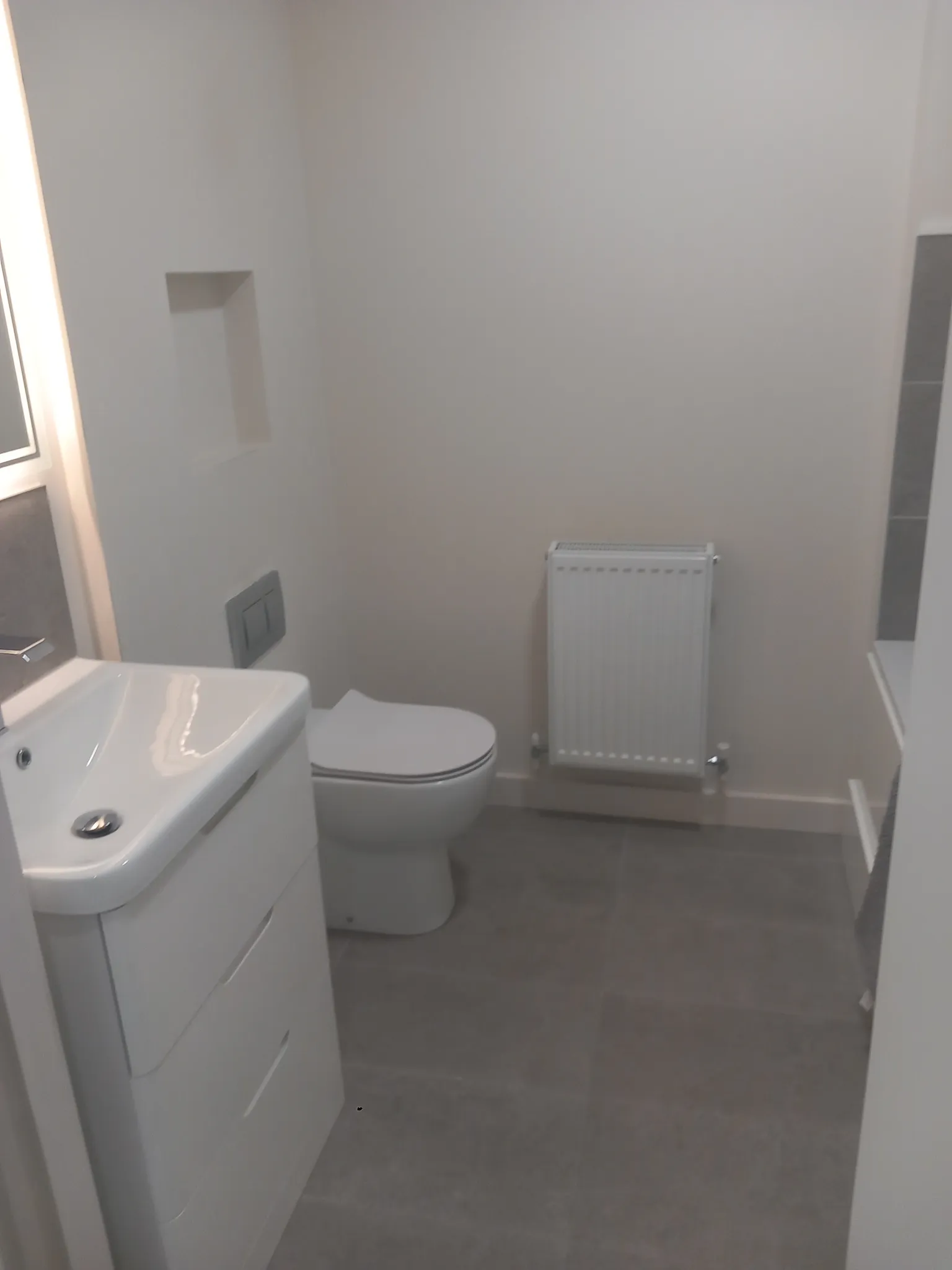 Small bathroom showing a sink with cabinet, a toilet, a wall radiator, tiled floor and a recessed wall niche.