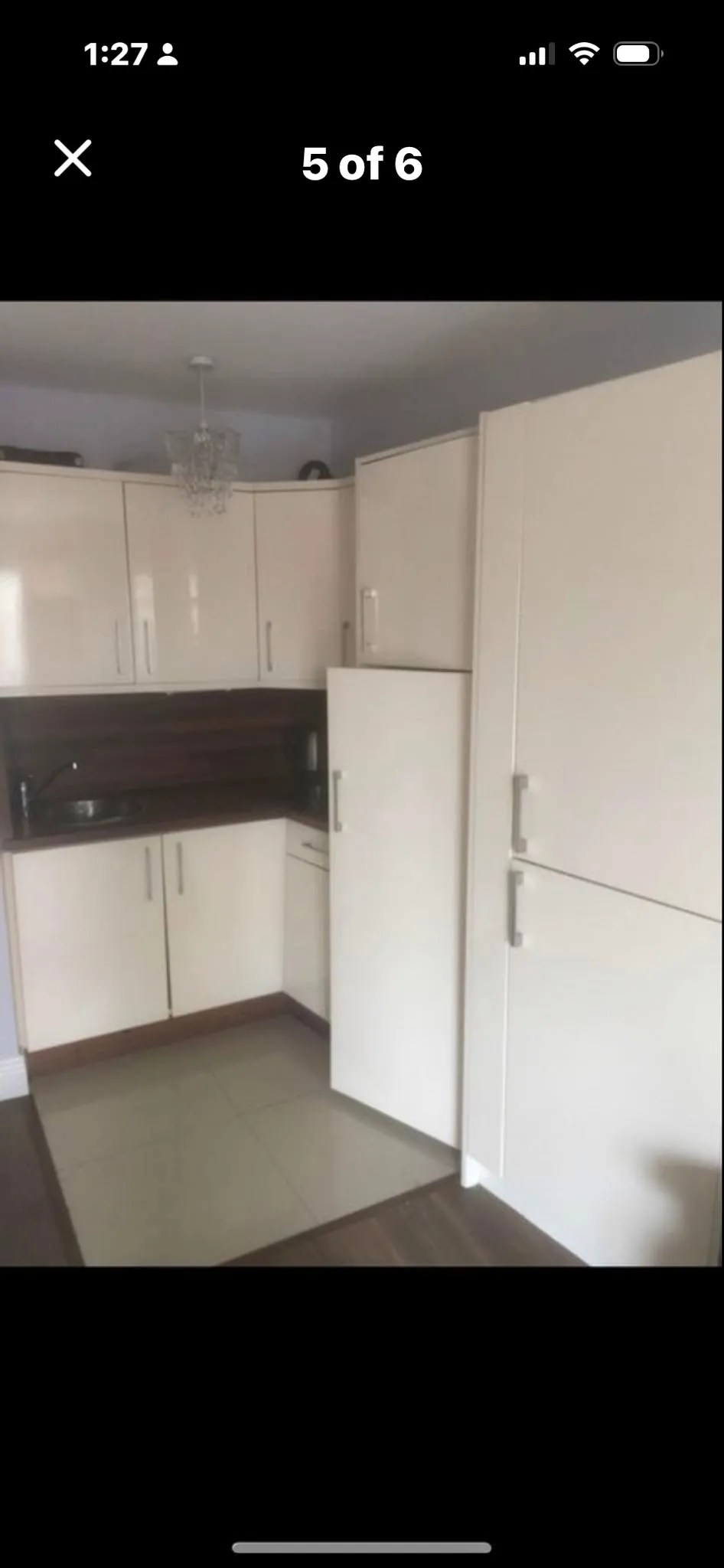 Kitchen corner with white cabinets, dark wood backsplash and countertop, small round sink, and a tall cabinet with refrigerator door.