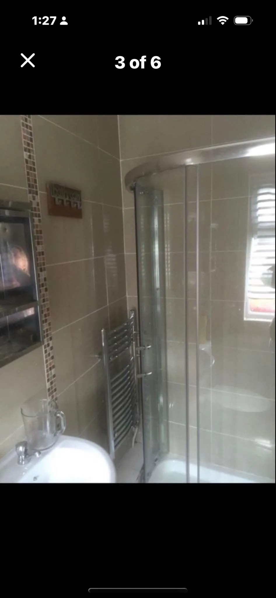 Bathroom with a curved glass shower enclosure, wall tiles, a heated towel rail, a sink basin and a small window with blinds.