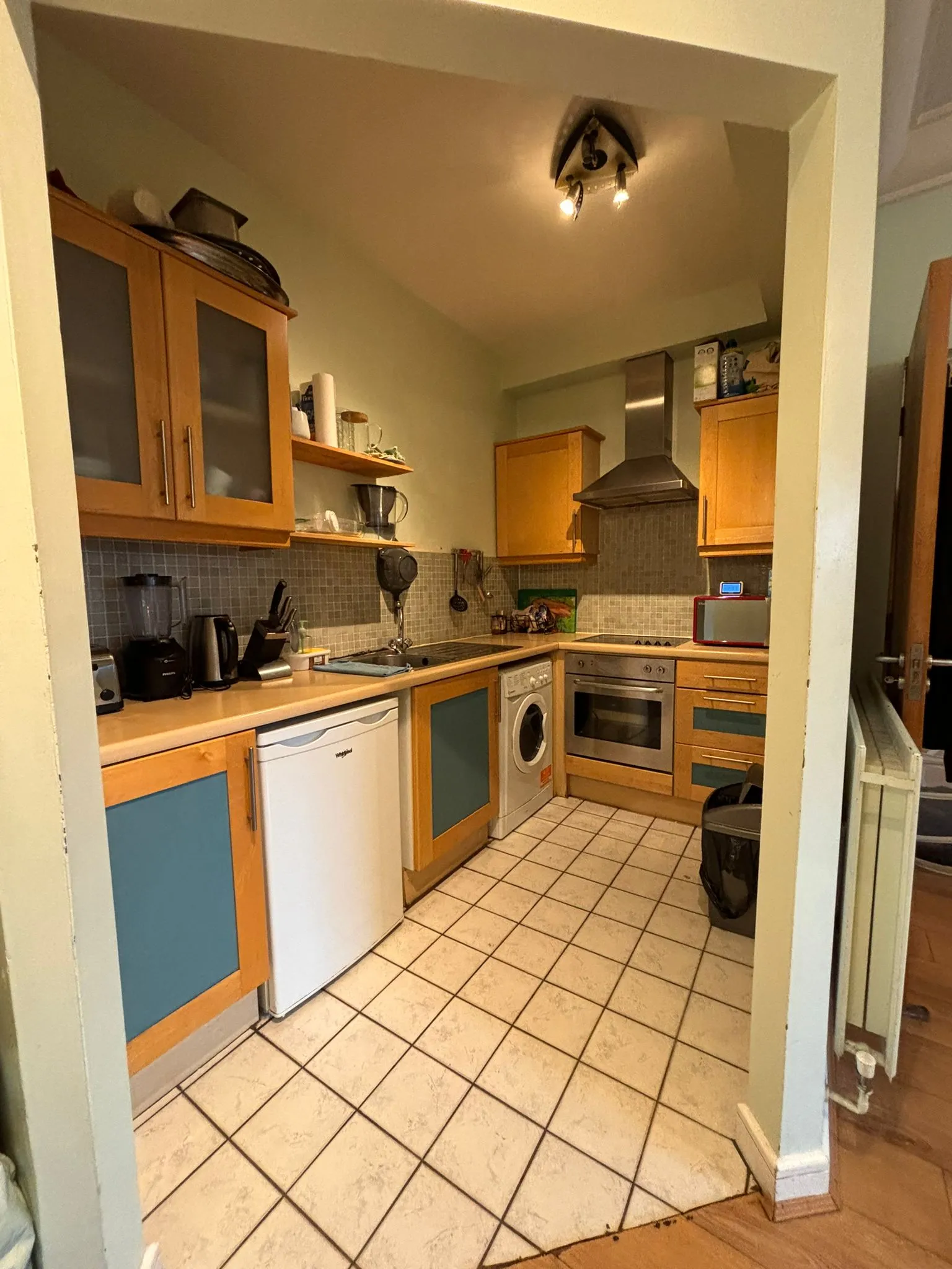 Kitchen with wooden cabinets, tiled floor, countertop, sink, washing machine and built-in oven.