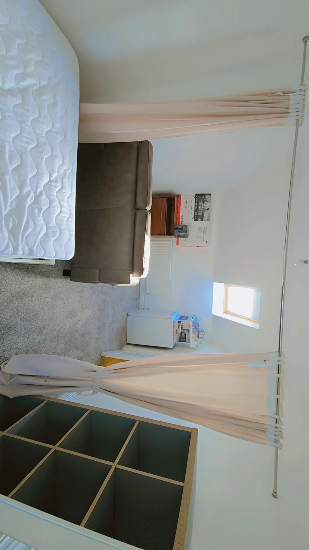 Bedroom with loft bed, white quilted mattress, brown headboard, wooden ladder, window with natural light, and storage shelving below